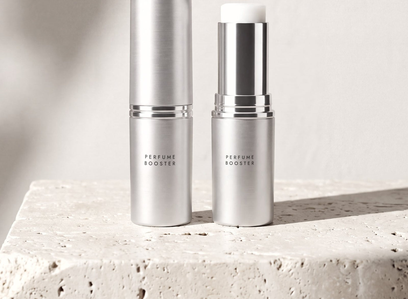 The Parfume Booster balm stick, open and closed, on a stone block